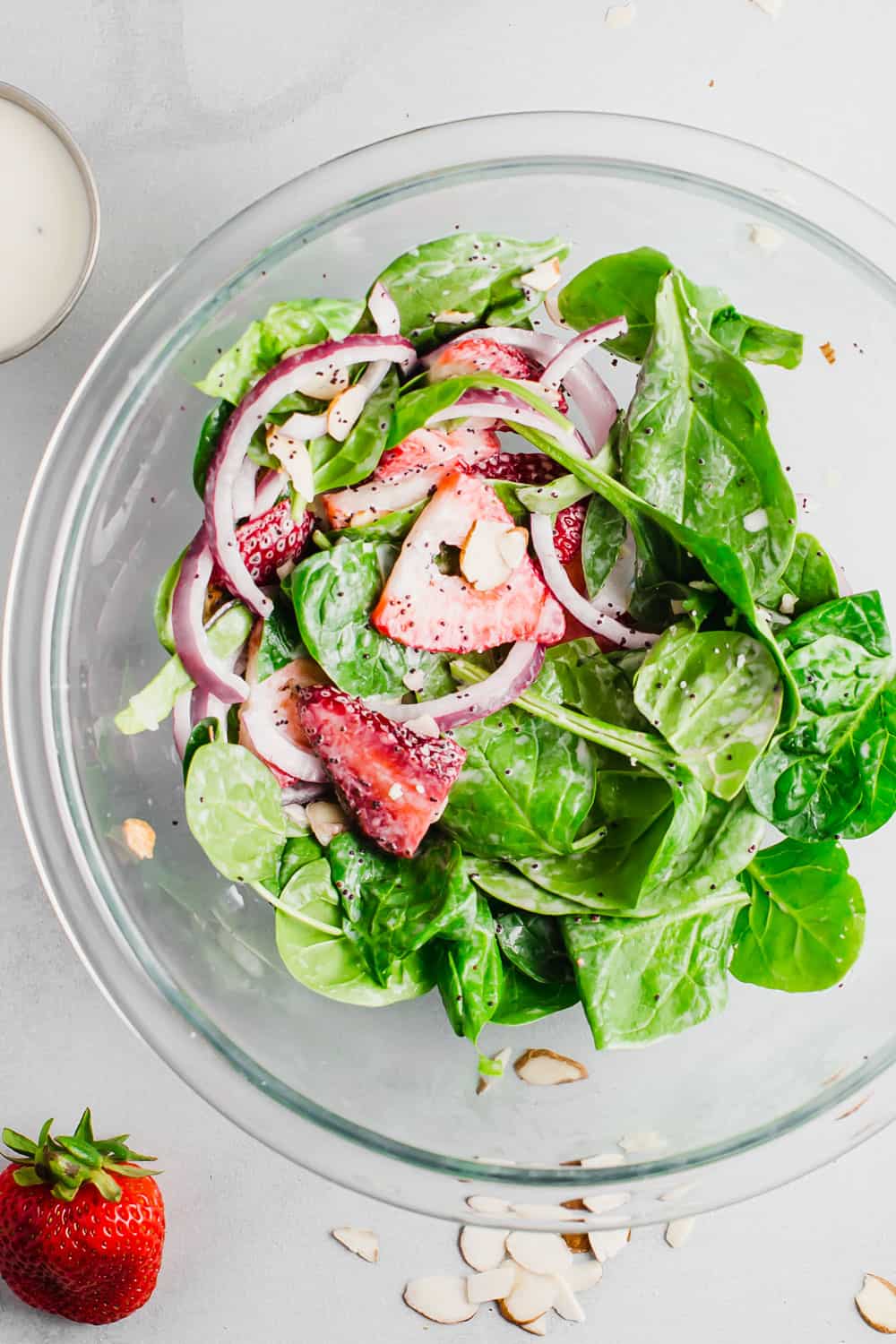 Strawberry spinach saladย is a perfect combination of fresh spinach, juicy strawberries, crunchy onions, and soft feta cheese; all tossed together with a creamy poppyseed dressing! All the flavor, texture, andย deliciousness in one bowl! Spinach salad being mixed with poppyseed dressing in a clear bowl.