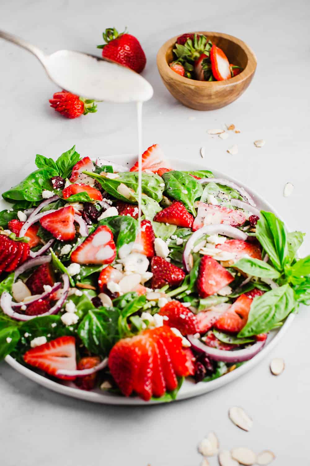 Strawberry spinach saladย is a perfect combination of fresh spinach, juicy strawberries, crunchy onions, and soft feta cheese; all tossed together with a creamy poppyseed dressing! All the flavor, texture, andย deliciousness in one bowl! Poppyseed dressing being drizzled into a bowl of strawberry spinach salad.