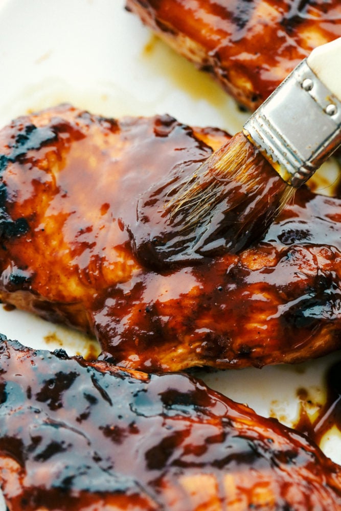 This grilled BBQ chicken is a simple to make tender chicken that's coated in a sweet homemade barbecue sauce that comes through with great flavor in every bite!ย You will be making this weekly after you see what a huge hit it is! Brushing barbecue sauce on grilled chicken.