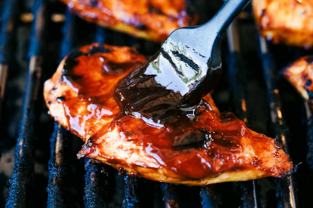 This grilled BBQ chicken is a simple to make tender chicken that's coated in a sweet homemade barbecue sauce that comes through with great flavor in every bite!ย You will be making this weekly after you see what a huge hit it is! Brushing barbecue sauce on chicken while it is grilling.