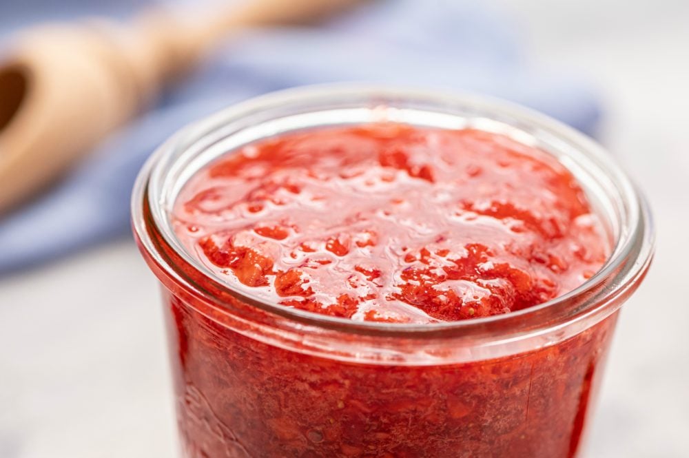 Homemade Strawberry Freezer Jam is a sweet and chunky jam that you can make quickly and enjoy for up to a year!ย Once you see how easy it is to make this strawberry jam, you will never buy it from a store again! Upclose photo of the strawberry jam in a glass jar.