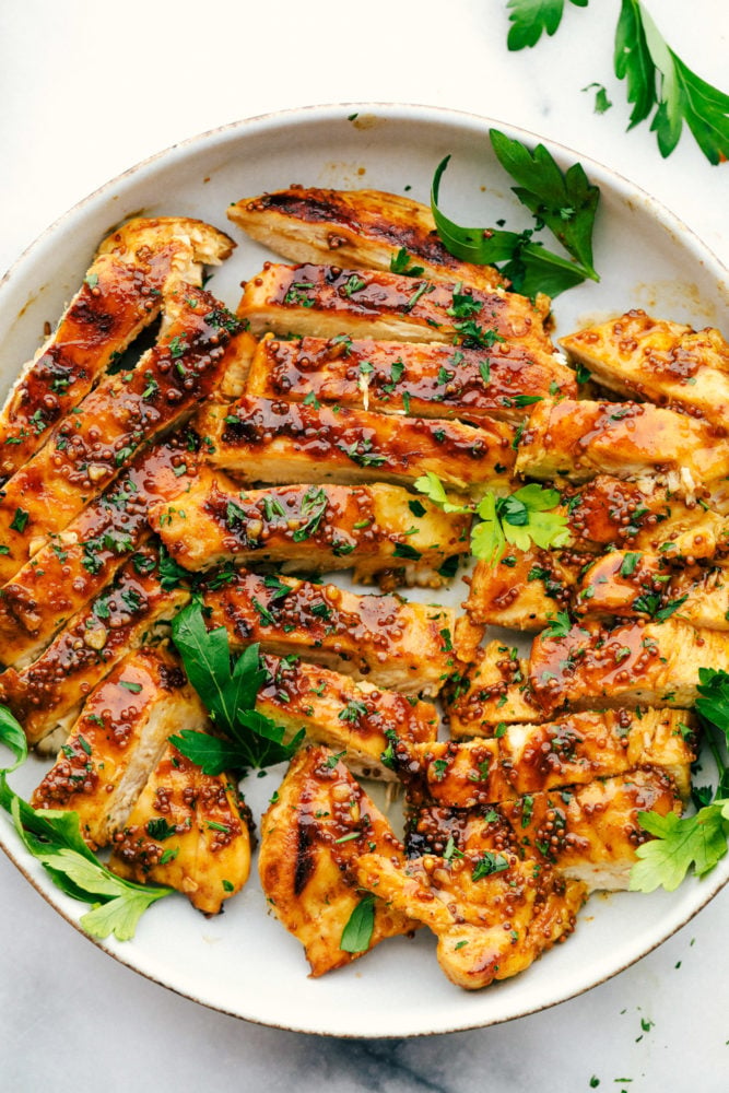 Grilled Honey Mustard chicken is tender and juicy grilled chicken covered in a sweet and tangy sauce with a punch of spice. It is simple to prepare and so flavorful. The fresh and perfectly balanced flavors of the honey mustard will be a staple in your summer BBQ plans! Honey mustard chicken grilled and sliced up on a white plate.