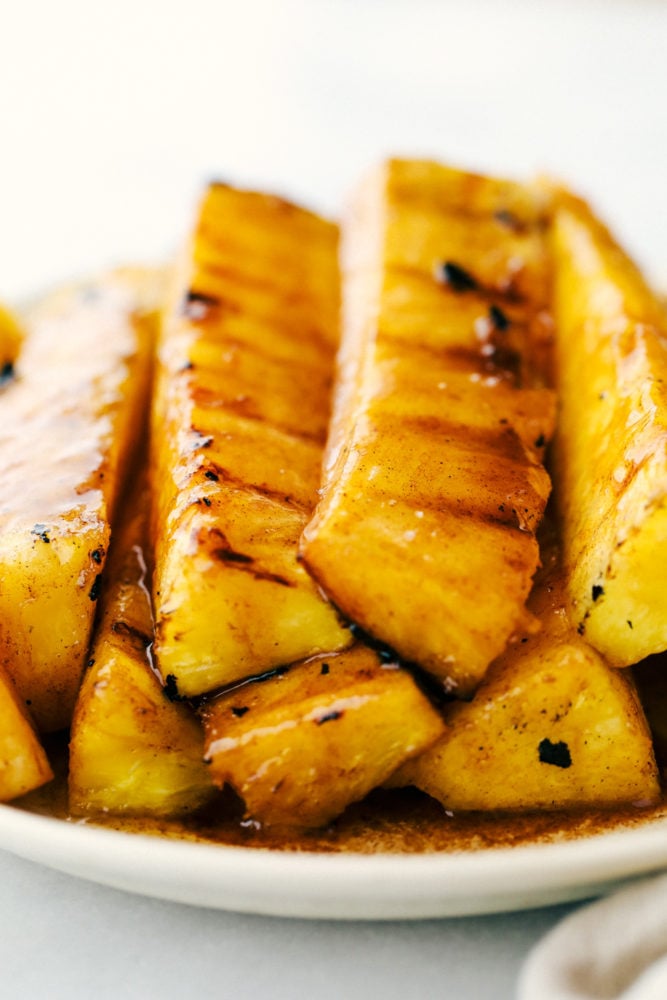 Pineapple spears that get coated in a buttery brown sugar cinnamon glaze and caramelize on the grill! Thisย will be one of the most amazing sides that you grill this summer! Pineapple stacked on top of each other on a white plate.