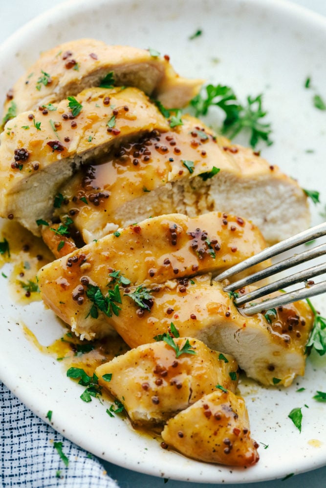 Honey Butter Baked Chicken is a rich and flavorful dinner that has tender baked chicken made with only four ingredients! The blend of honey and butter is the perfect combination for a flavorful chicken dinner.ย Baked honey butter chicken cut up on a white plate with a fork stabbing a piece of chicken.