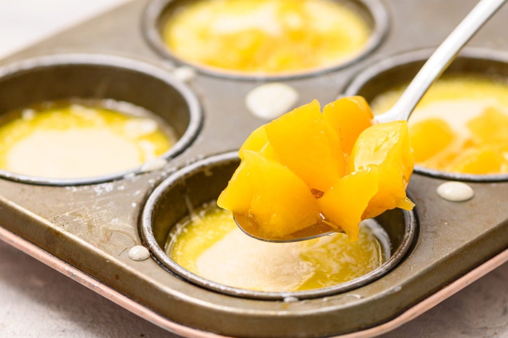 Mini Peach cobbler is the perfect warm, sweet dessert to satisfy any sweet tooth.ย The flaky crust and sweet fruit filling will have you liking the spoon! Especially when you top it with some creamy vanilla ice cream! Adding peaches into the muffin tins with butter and cobbler mix.