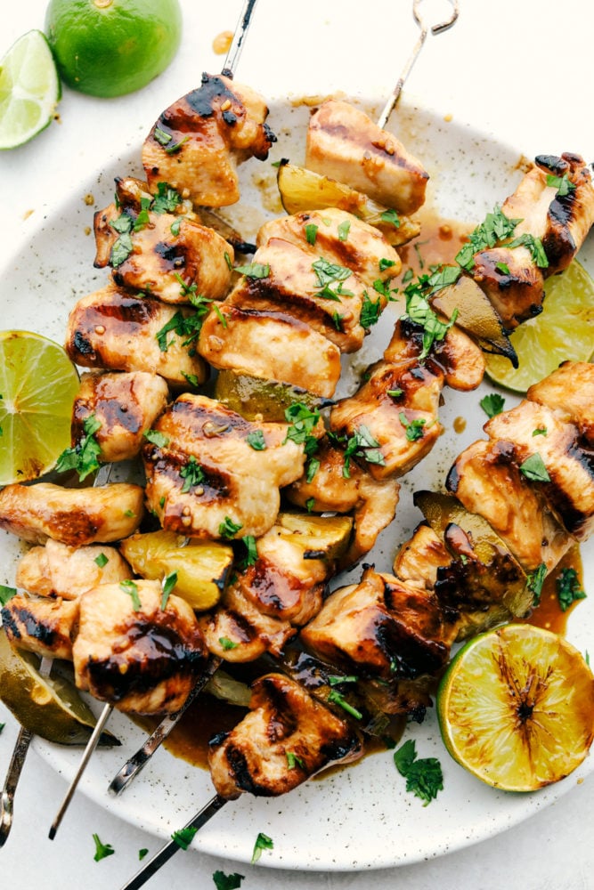 Grilled Key Lime Chicken is tender and juicy chicken drenched in key lime flavor and grilled to perfection on a skewer. It is quick and easy to make and enjoy with your family on a warm summer night! Grilled Key Lime Chicken on skewers on a white plate with fresh cut lemon on the side.