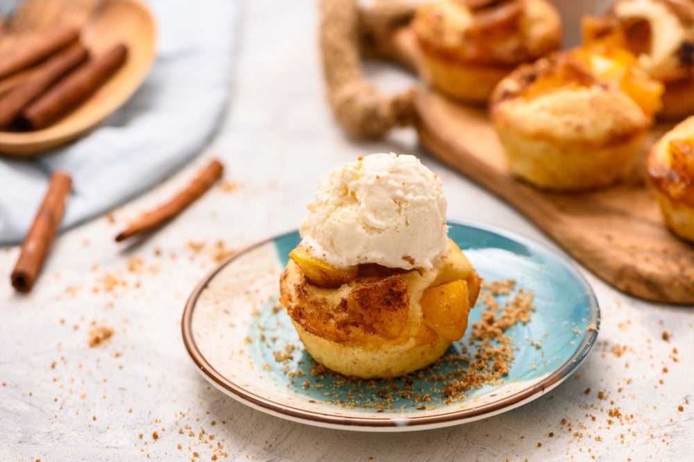 Mini Peach cobbler is the perfect warm, sweet dessert to satisfy any sweet tooth.ย The flaky crust and sweet fruit filling will have you liking the spoon! Especially when you top it with some creamy vanilla ice cream! Mini peach cobbler on a plate with cinnamon sticks around and the mini peach cobbler topped with a scoop of vanilla ice cream.