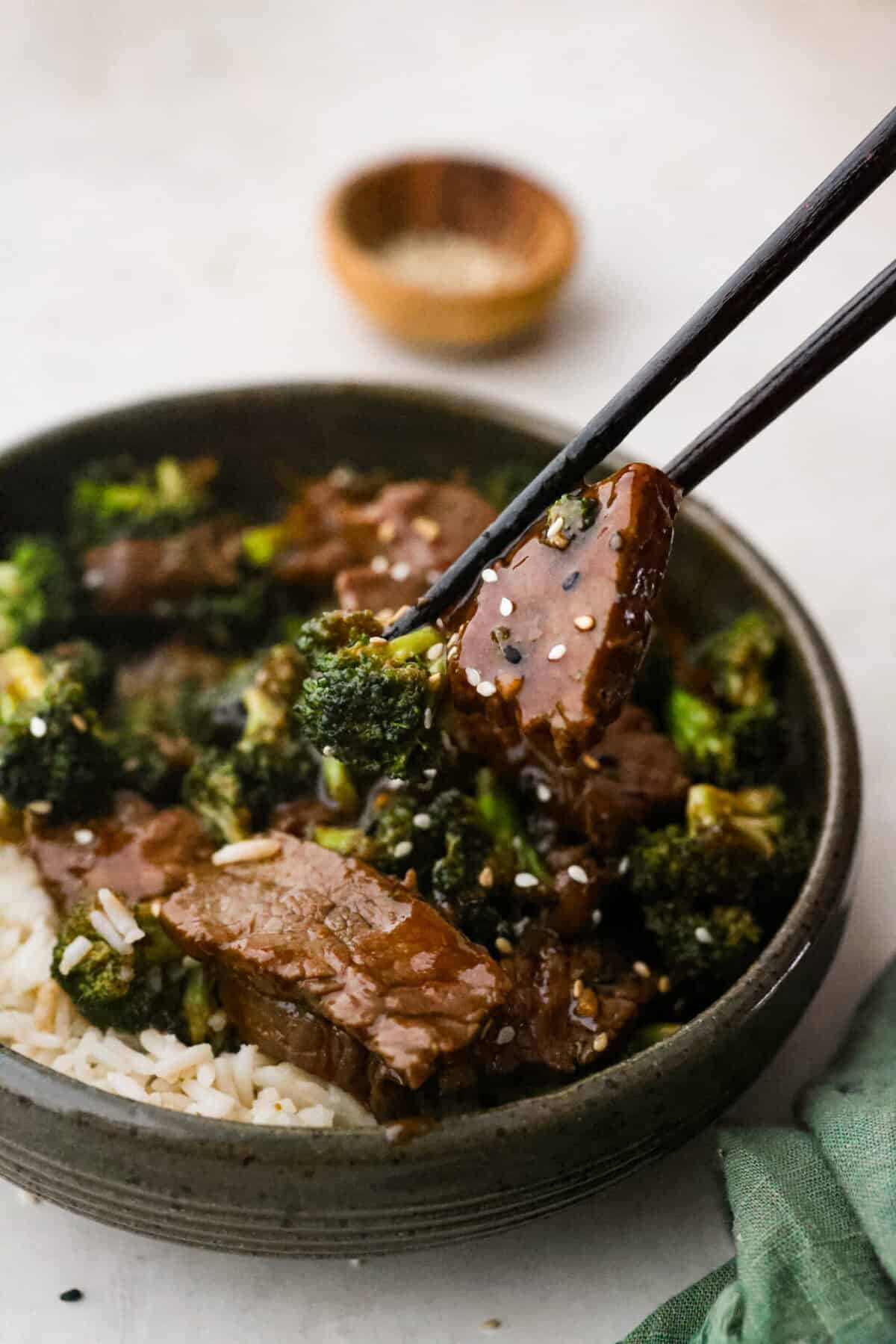 This Mongolian beef and broccoli recipe is the best P.F. Chang’s copycat recipe. You will love the combination of tender beef, vibrant broccoli and intensely flavorful sauce. Save yourself money while making your family happy with this quick and easy recipe. Side shot of someone taking a bit of Mongolian beef and broccoli with chop sticks from a plated dish.