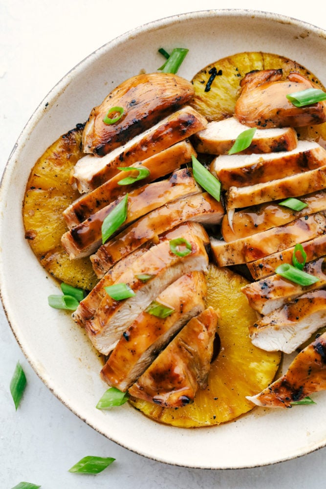 This Hawaiian chicken is marinated in a rich, flavorful sweet and savory sauce that tenderizes the chicken then grilled to perfection. Imagine being in Hawaii with this summertime favorite!ย Grilled Hawaiian chicken breast cut into slices over top grilled pineapple on a white plate.
