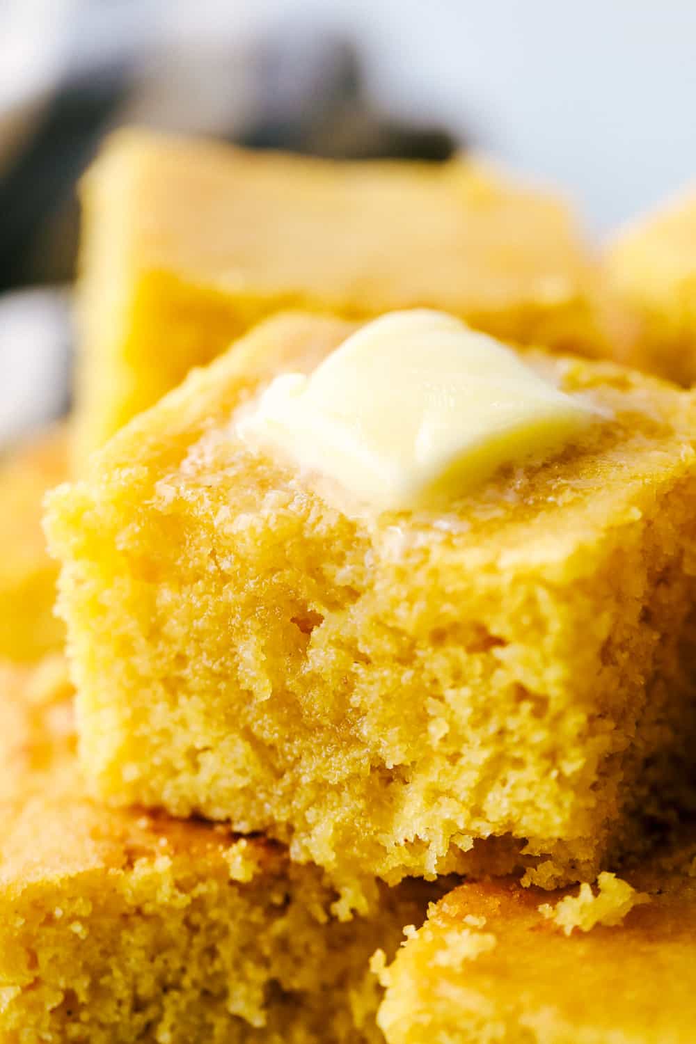 This Homemade Cornbread is made from scratch and is the best of the best. It has the most perfect texture and is packed with flavor. I know you won't be able to stop at just one piece! A closeup of a slice of cornbread with butter on top.