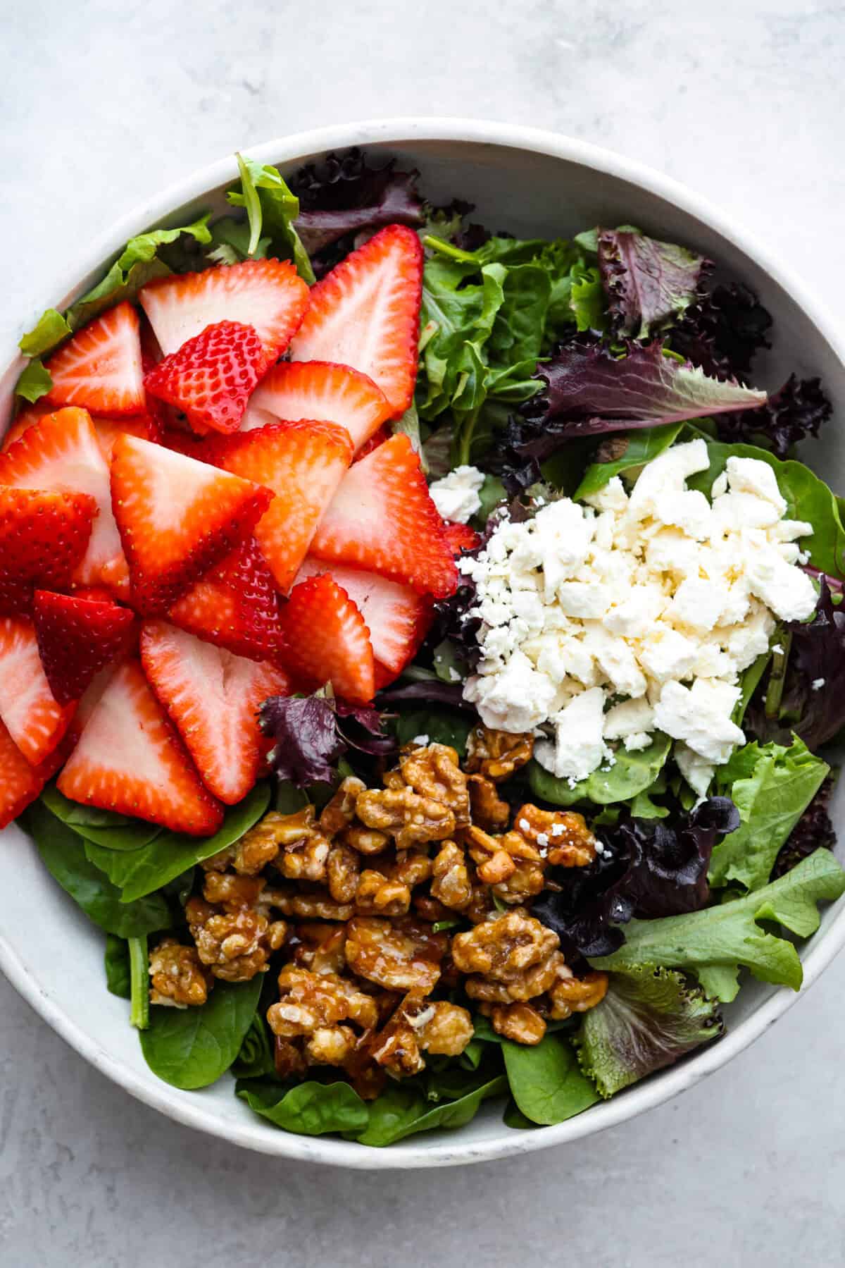 This Strawberry Spinach Salad is my FAVORITE spring salad! The juicy strawberries and candied walnuts add the best texture. Toss it with my creamy poppyseed dressing and you have the prettiest salad at the table! Overhead shot of all of the strawberry spinach salad ingredients together in a bowl.