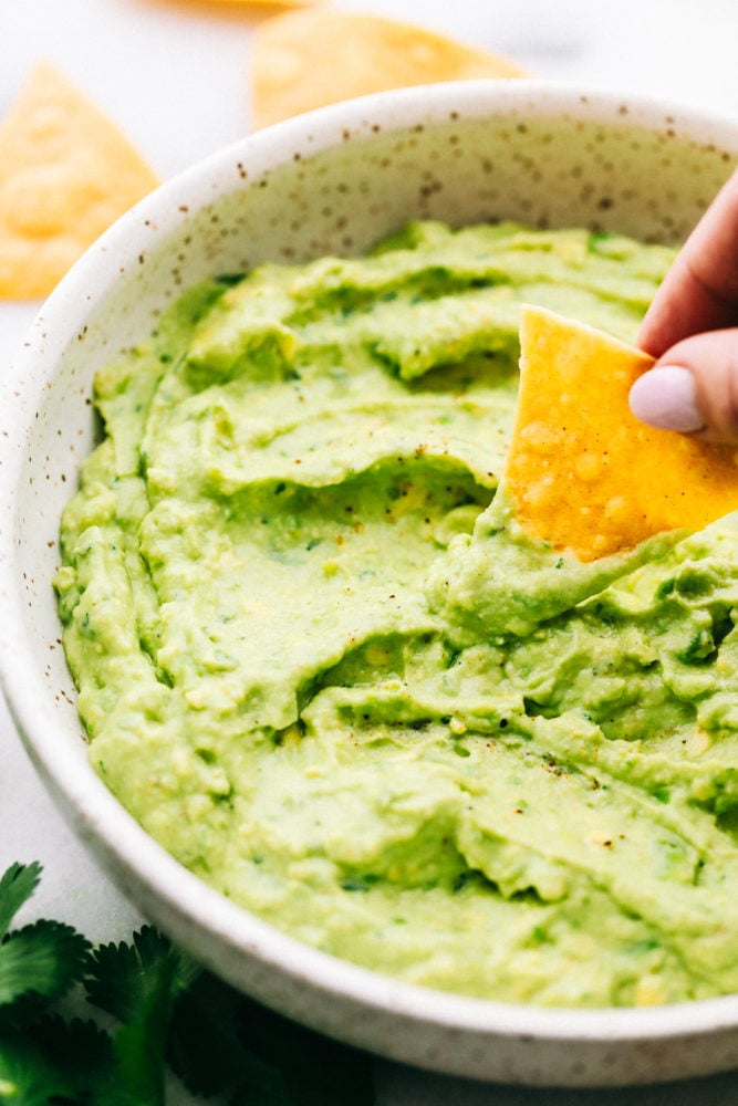 This Creamy Avocado dip is one of the best dips that I have EVER had! ย Creamy, healthy, and full of flavor, you won't be able to get enough! Creamy avocado dip in a bowl with a chip being dipped in and having a little bit of avocado yogurt dip on a chip.