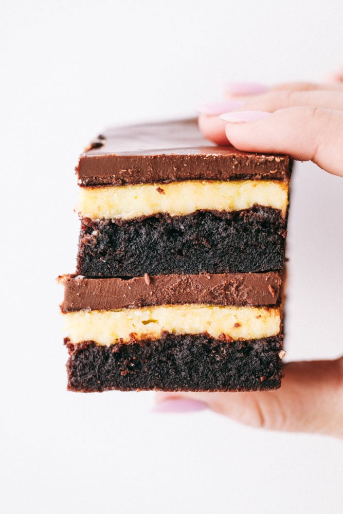 This delicious Hershey's chocolate cheesecake brownies are layered with a moist, homemade chocolate cake with a creamy cheesecake filling topped with a thick Hershey chocolate layer making this irresistible. Heaven on a plate! Two Hershey's chocolate cheesecake brownies stacked on top of each other being held in the air.