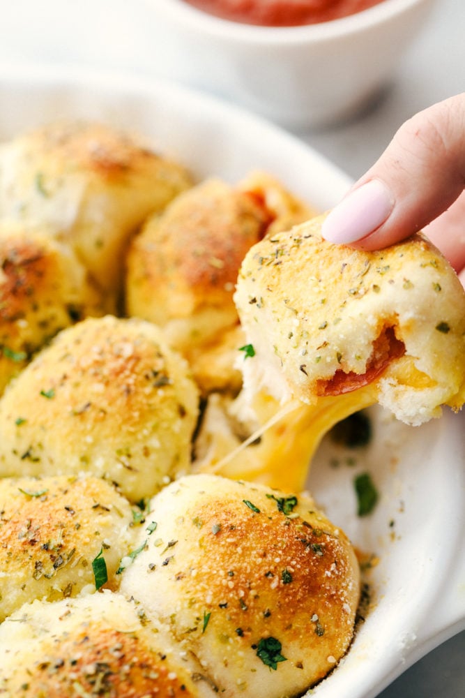 These pizza bites taste just like pizza using a flattened biscuit and stuffing it full of cheese, pepperoni then baking until golden brown on top. Stuffed pizza bites are the hit of our house! A pizza bite pulled apart from the pan seeing the cheese and pepperoni in the middle.