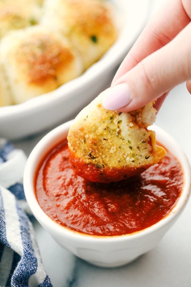 These pizza bites taste just like pizza using a flattened biscuit and stuffing it full of cheese, pepperoni then baking until golden brown on top. Stuffed pizza bites are the hit of our house! A pizza bite being dipped in marinara sauce.