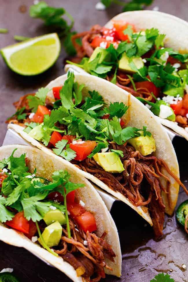 Flank steak that is rubbed in spices and slow cooks with peppers, jalapeรฑo, and onions all day to tender and juicy perfection! This recipe is easy and will become a family favorite!ย flank steak tacos with cilantro garnished on top with limes on the side.