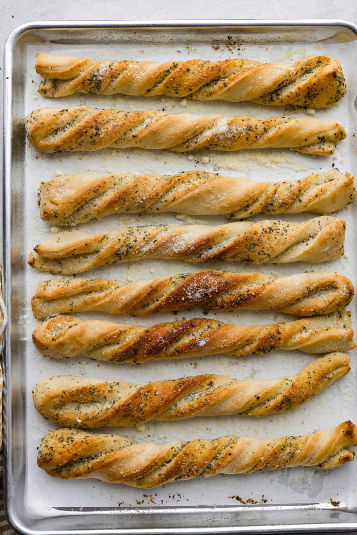 Homemade breadtwists have all the delicious buttery, garlic flavor of your favorite restaurant-quality breadsticks, but now they are unbelievably easy to make at home!ย The smell that fills your home will make you want to eat them straight out of the oven! Overhead shot of baked homemade breadtwists on a baking sheet.