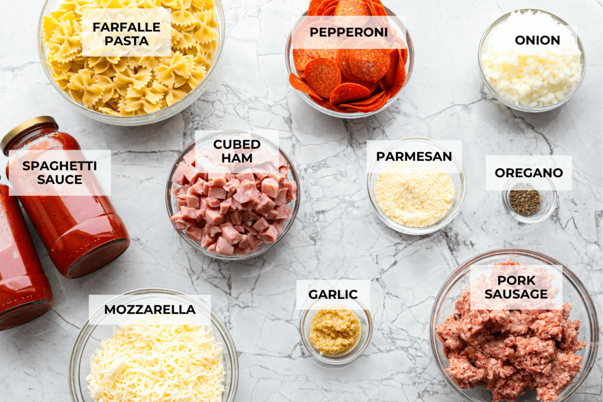 Cheesy pizza casserole combines rich tomato sauce, savory garlic, melted cheese, ham, sausage, and pepperoni. It has all the classic pizza flavors you love in a comforting casserole. Itโs a hearty, satisfying meal thatโs sure to hit the spot! Overhead shot of labeled ingredients.
