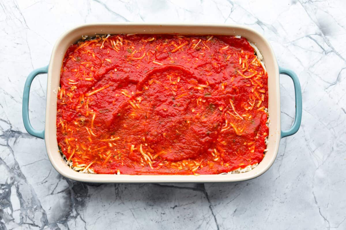 Cheesy pizza casserole combines rich tomato sauce, savory garlic, melted cheese, ham, sausage, and pepperoni. It has all the classic pizza flavors you love in a comforting casserole. Itโs a hearty, satisfying meal thatโs sure to hit the spot! Overhead shot of baking dish with pizza casserole layers up until the pizza sauce.