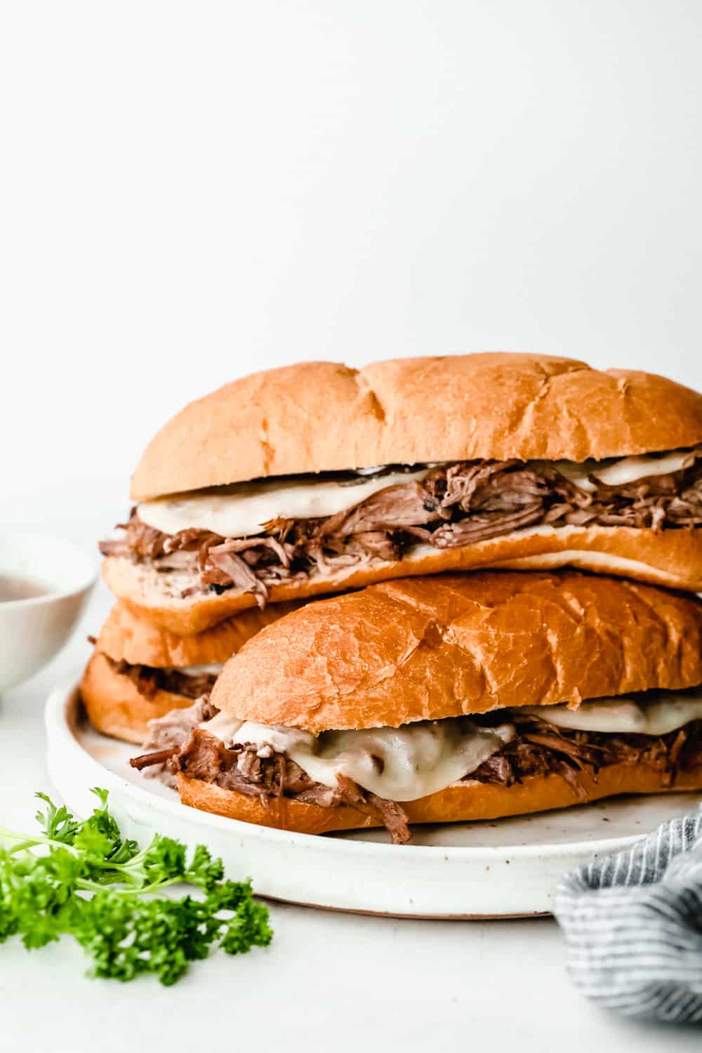 Slow Cooker French Dip Sandwiches are filled with tender chunks of roast beef with thin slices of melted mozzarella cheese all held together by a soft hoagie bread all dipped in au jus sauce. This warm, savory and comforting sandwich is a MUST! slow cooker French dip sandwiches stacked together