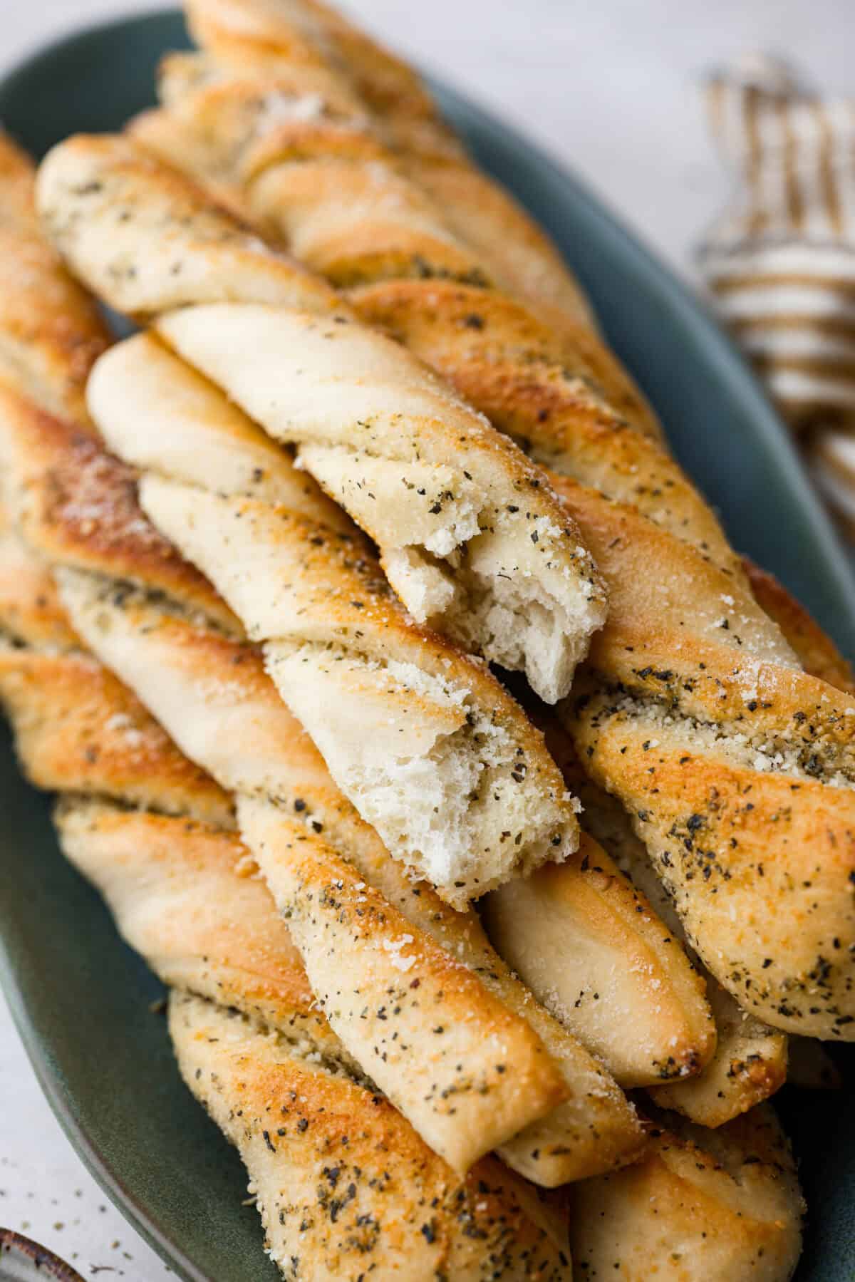 Homemade breadtwists have all the delicious buttery, garlic flavor of your favorite restaurant-quality breadsticks, but now they are unbelievably easy to make at home!ย The smell that fills your home will make you want to eat them straight out of the oven! Close up shot of homemade breadtwists stacked on a plate.