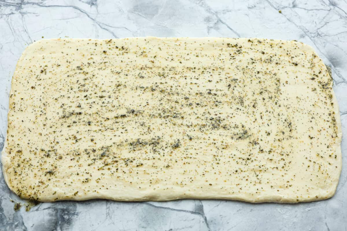 Homemade breadtwists have all the delicious buttery, garlic flavor of your favorite restaurant-quality breadsticks, but now they are unbelievably easy to make at home!ย The smell that fills your home will make you want to eat them straight out of the oven! Overhead shot of bread dough rolled out in a large rectangle with garlic butter spread over the top.