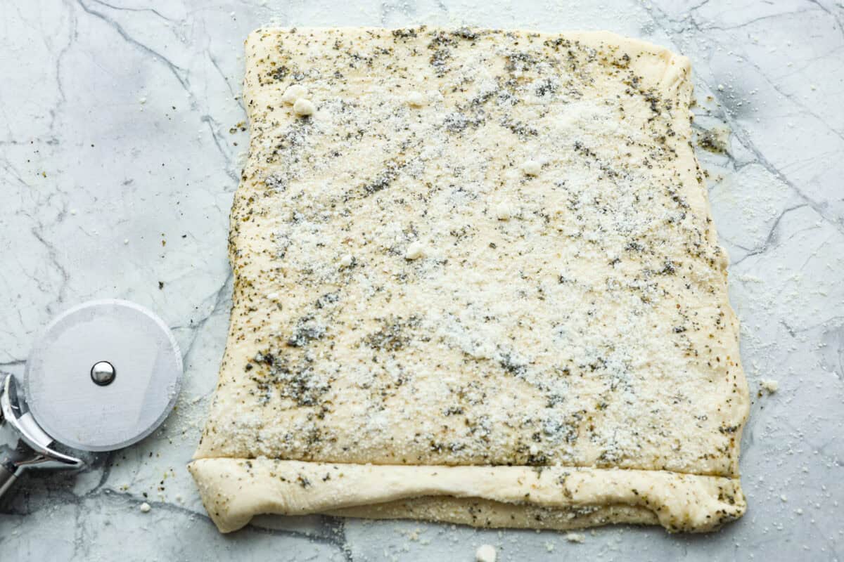 Homemade breadtwists have all the delicious buttery, garlic flavor of your favorite restaurant-quality breadsticks, but now they are unbelievably easy to make at home!ย The smell that fills your home will make you want to eat them straight out of the oven! Overhead shot of homemade breadtwists dough folded in half with garlic butter and cheese spread over the top.