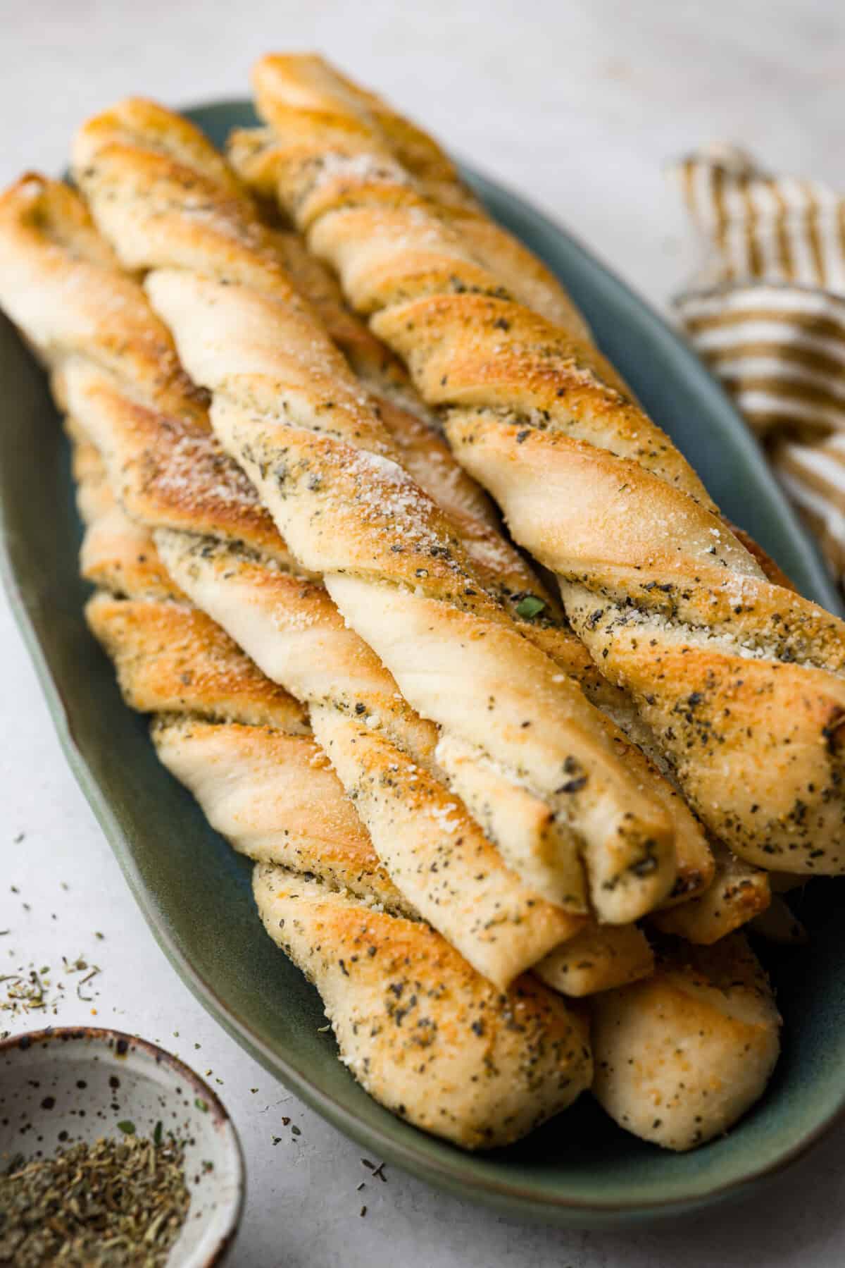 Homemade breadtwists have all the delicious buttery, garlic flavor of your favorite restaurant-quality breadsticks, but now they are unbelievably easy to make at home!ย The smell that fills your home will make you want to eat them straight out of the oven! Angle shot of homemade breadtwists stacked on a plate.