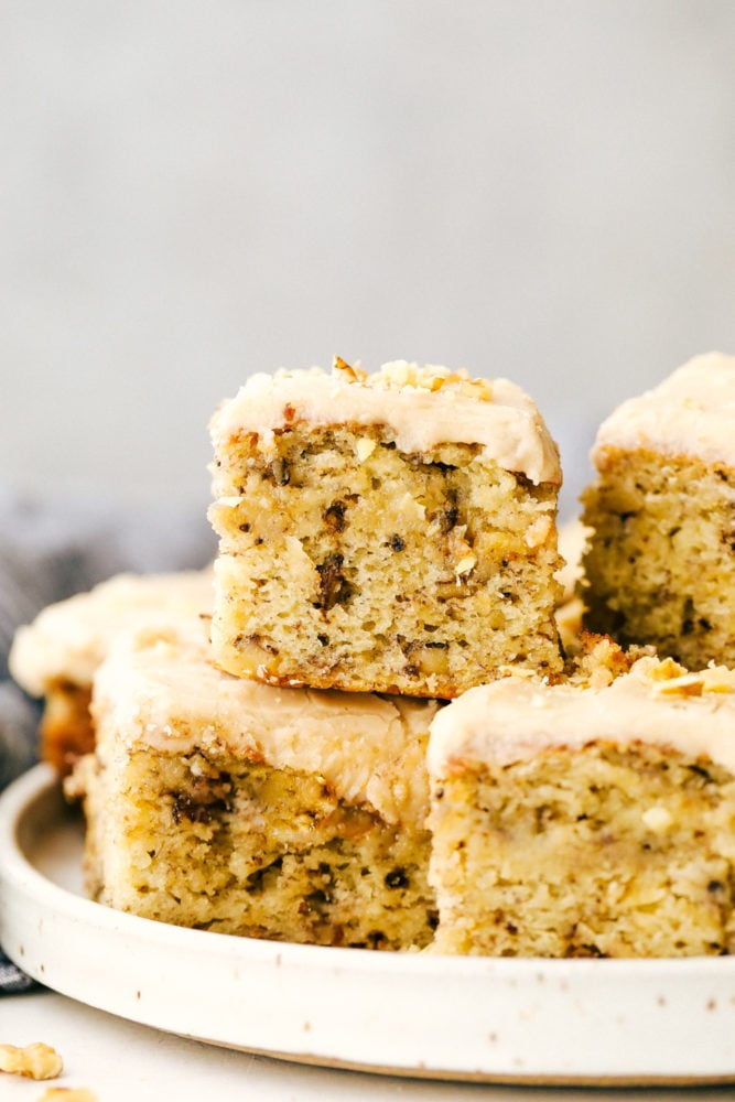 Banana bread bars are moist and flavorful and land somewhere between a cake and a bread with the most amazing brown butter frosting on top! Great for breakfast or an afternoon treat with a cup of coffee, both the texture and flavor are crave-worthy! Banana bread bars on a white plate stacked on top of each other.
