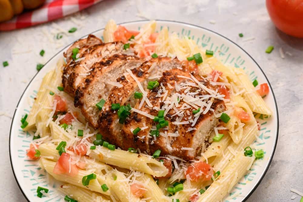 Cajun chicken pasta is so creamy and rich with a spicy kick that keeps you digging in for more.ย It is a great way to mix up your usual weekly meals.ย The cajun spice will wake up your tastebuds and your night! It is a meal you will be excited to make and even more excited to eat! Cajun chicken pasta on a plate garnished with shredded parmesan.