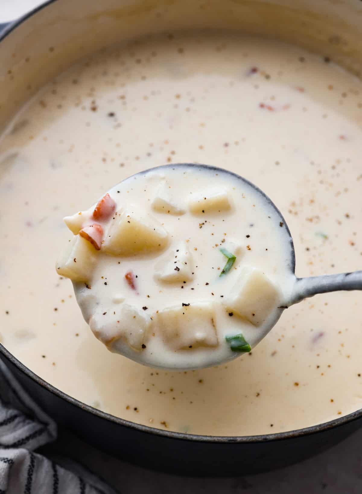 Creamy Potato Soup is the ultimate comfort food. It has a velvety, creamy base with blended potato, tender potato bites, onions, and garlic, all topped with crispy bacon! It's the perfect meal to cozy up with on a cold day. Close up shot of a ladle full of creamy potato soup over the pot full of soup.
