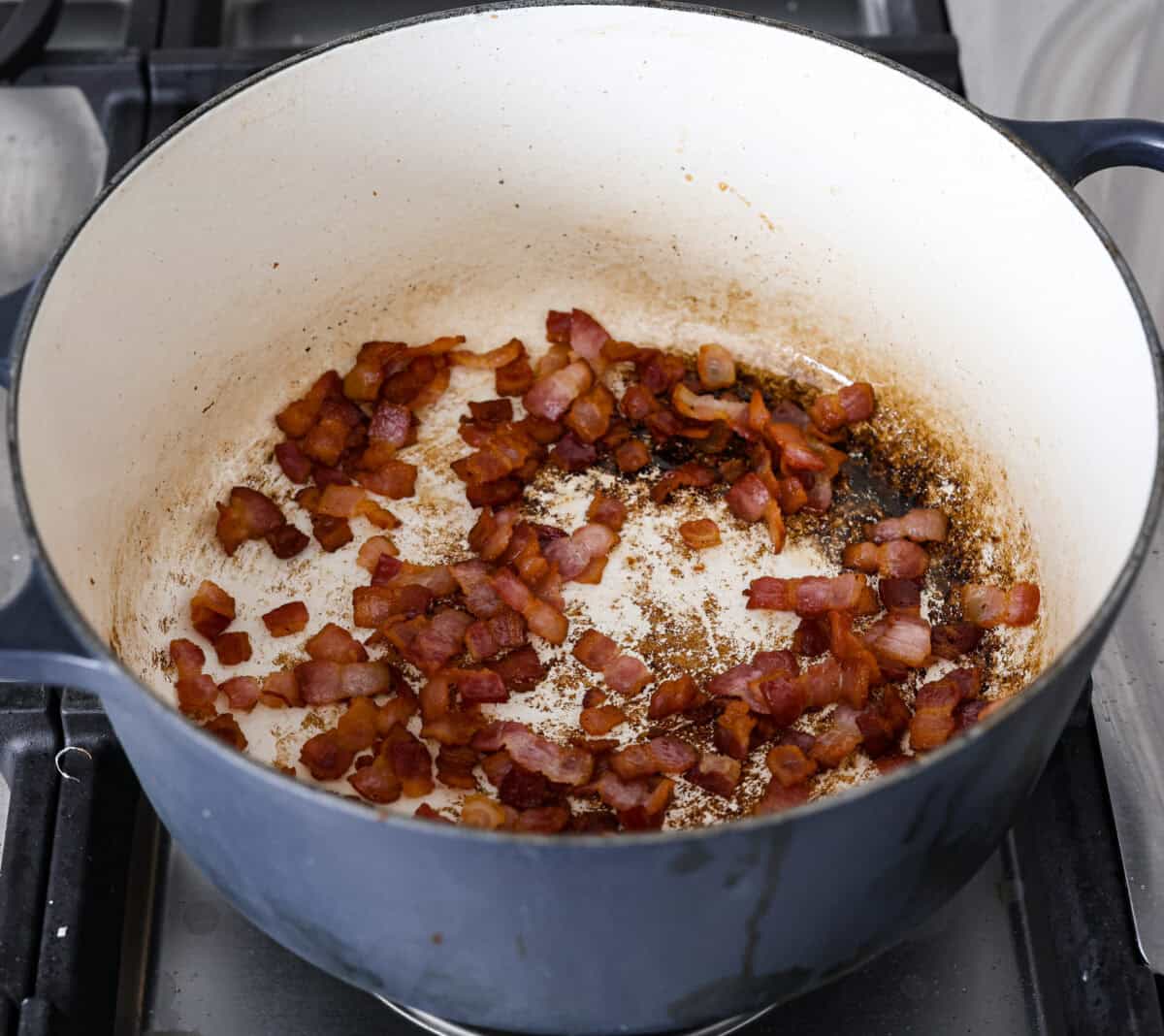 Creamy Potato Soup is the ultimate comfort food. It has a velvety, creamy base with blended potato, tender potato bites, onions, and garlic, all topped with crispy bacon! It's the perfect meal to cozy up with on a cold day. Angle shot of bacon cooking in a large pot.
