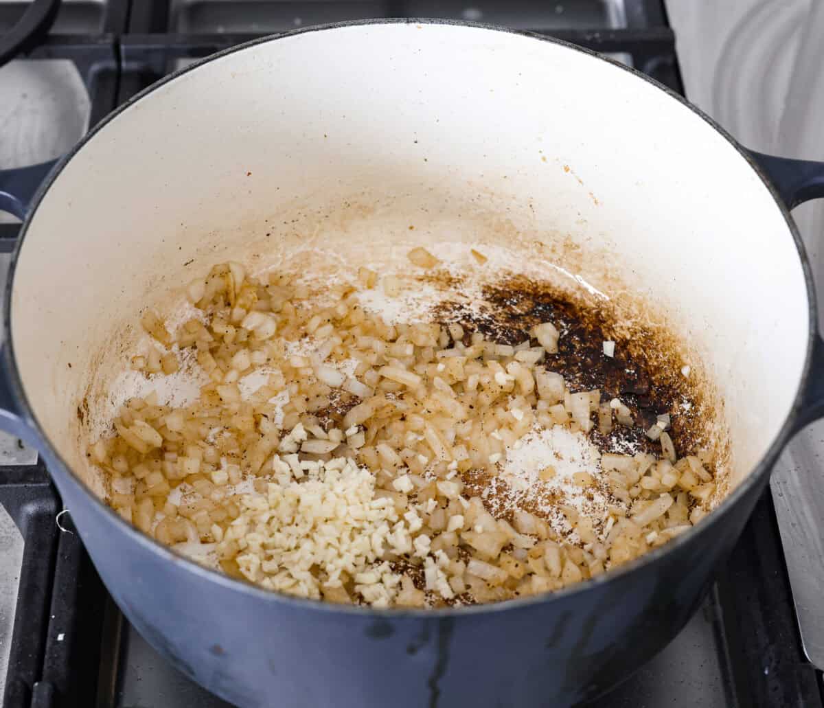 Creamy Potato Soup is the ultimate comfort food. It has a velvety, creamy base with blended potato, tender potato bites, onions, and garlic, all topped with crispy bacon! It's the perfect meal to cozy up with on a cold day. Angle shot of onions and garlic cooking in a large pot.