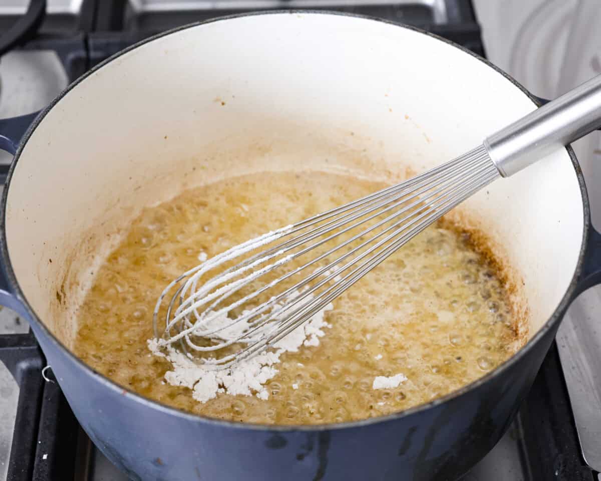 Creamy Potato Soup is the ultimate comfort food. It has a velvety, creamy base with blended potato, tender potato bites, onions, and garlic, all topped with crispy bacon! It's the perfect meal to cozy up with on a cold day. Angle shot of someone whisking four into the melted butter in the pot.