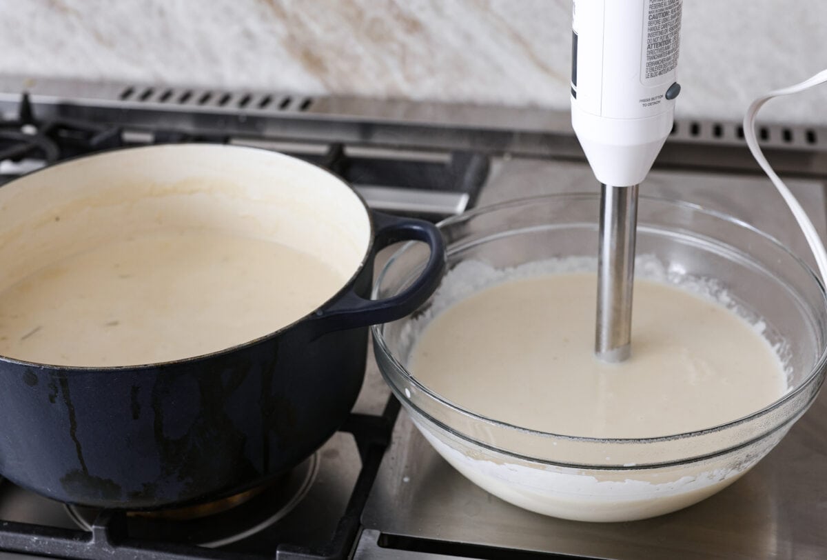 Creamy Potato Soup is the ultimate comfort food. It has a velvety, creamy base with blended potato, tender potato bites, onions, and garlic, all topped with crispy bacon! It's the perfect meal to cozy up with on a cold day. Side shot of half the soup mixture blended in a glass bowl with an immersion blender.