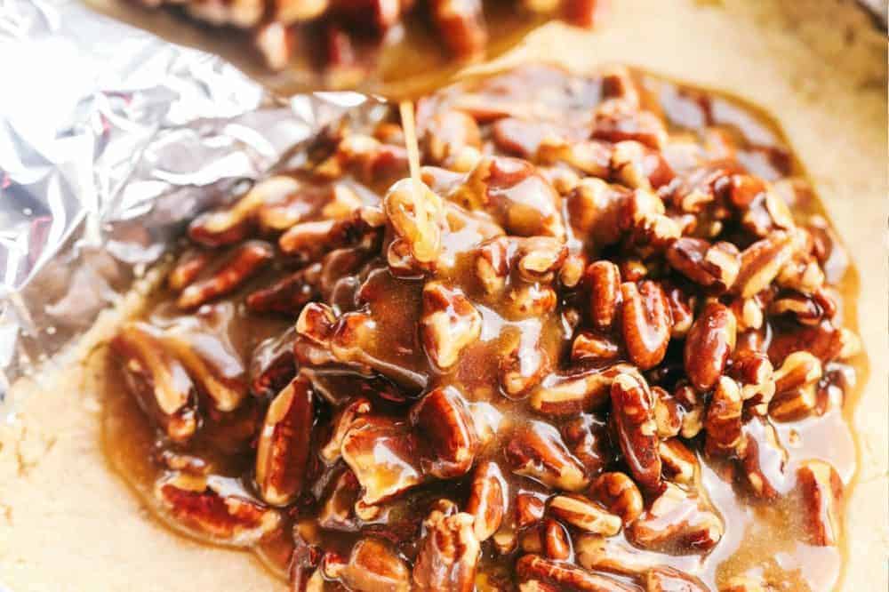 Best Ever Pecan Pie Bars takes the amazing pecan pie and transforms it into irresistible bars. A buttery shortbread crust that gets topped with a caramel pecan glaze, these are perfect for feeding a crowd! Pecan mixture being poured onto the crumb base.
