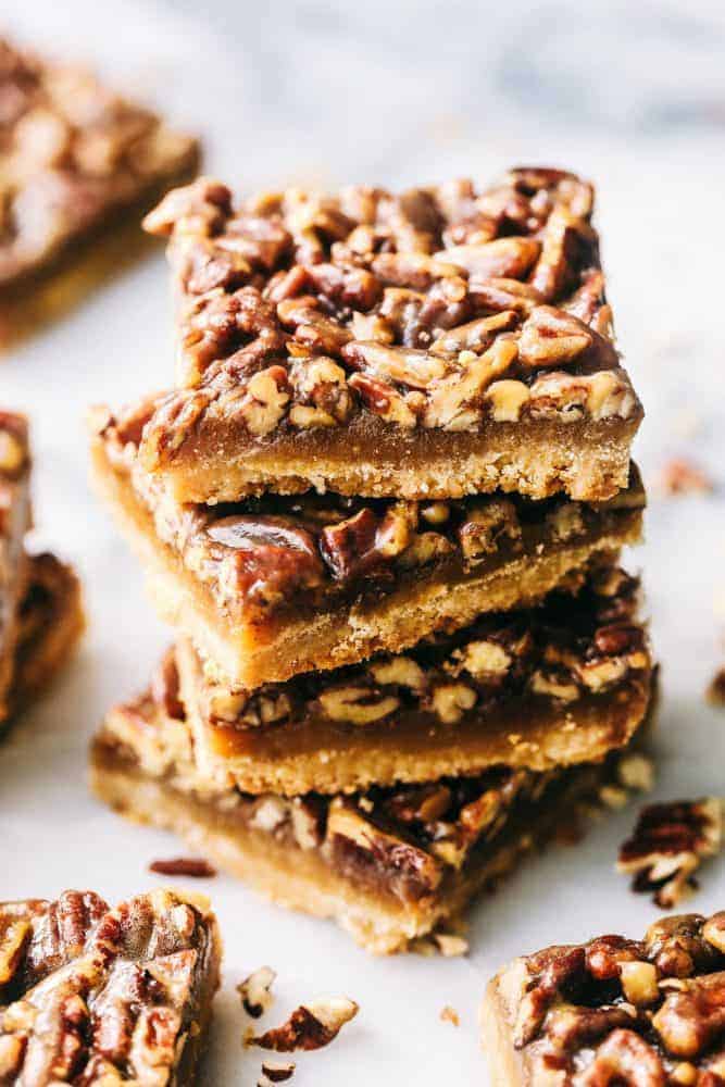 Best Ever Pecan Pie Bars takes the amazing pecan pie and transforms it into irresistible bars. A buttery shortbread crust that gets topped with a caramel pecan glaze, these are perfect for feeding a crowd! Pecan Pie Bars stacked on top of one another.