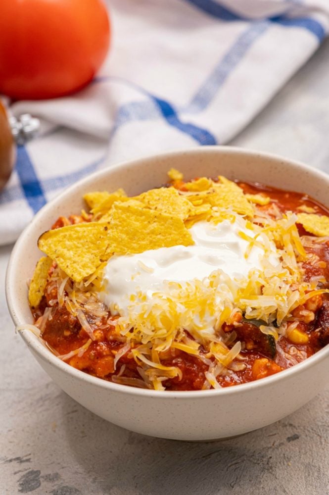 Skinny Taco Soup is jam packed with flavor and texture and is a comforting hearty meal your whole family will love! The meat and beans are super filling and the spices from the seasonings make your taste buds smile! Its the perfect complete meal all in one bowl! Skinny taco soup in a white bowl garnished with chips and cheese.