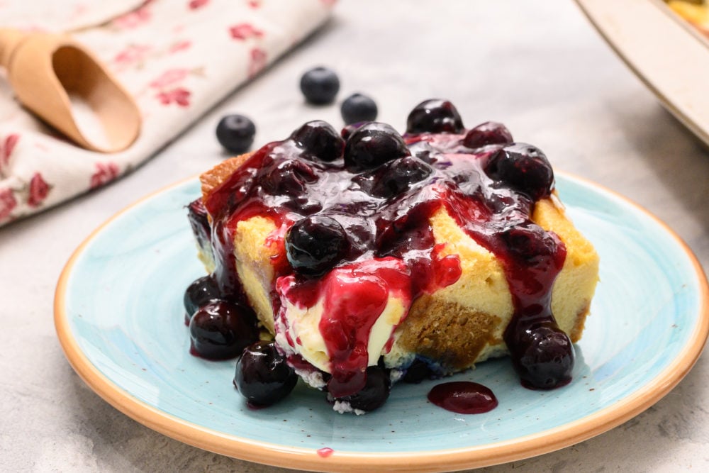 Warm, fruity, soft bites of breakfast perfection is what you get when you make this overnight blueberry french toast! I love going to bed knowing that when I wake up I will have breakfast ready to pop in the oven and enjoy! What a great way to start the day! Overnight blueberry French toast on a plate topped with blueberries and syrup.