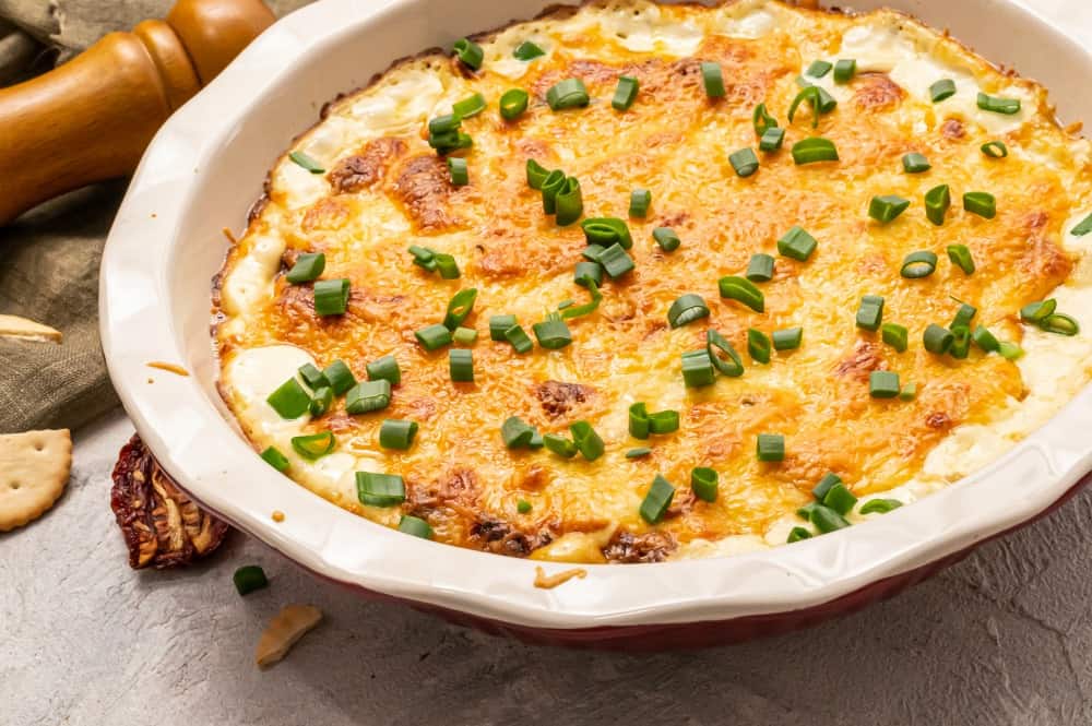 Asiago dip is super creamy and is loaded with flavor!ย There are just a few ingredients and simple, easy to follow steps.ย It has the perfect flavor combination, and trust me when I say one bite of this delicious dip will not be enough!ย It will get devoured in no time by anyone who tries it! Asiago dip in a white dish with scallions garnished over top.