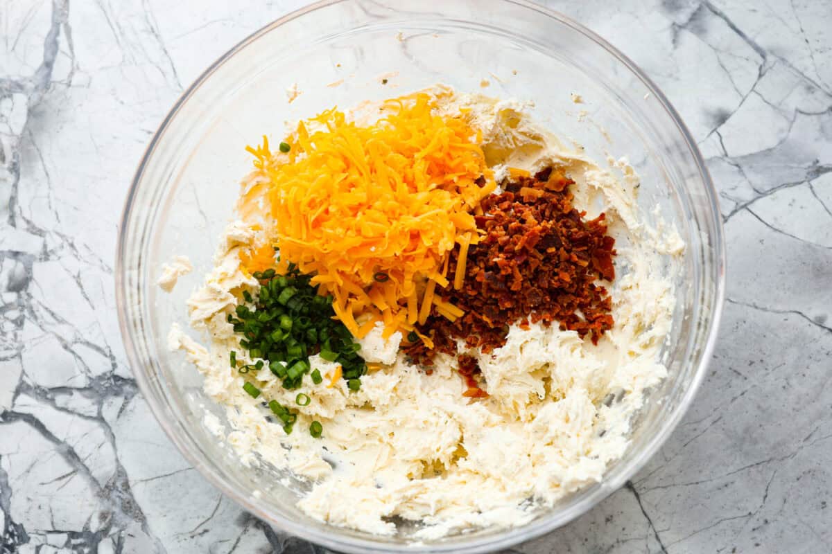 This bacon ranch cheese ball will be your favorite go-to appetizer! The winning combination of bacon, ranch seasoning, and cheddar cheese really stands out in this tasty cheese ball. Serve with crackers and watch everyone devour it! Second photo of the cheese ball ingredients added to the bowl.