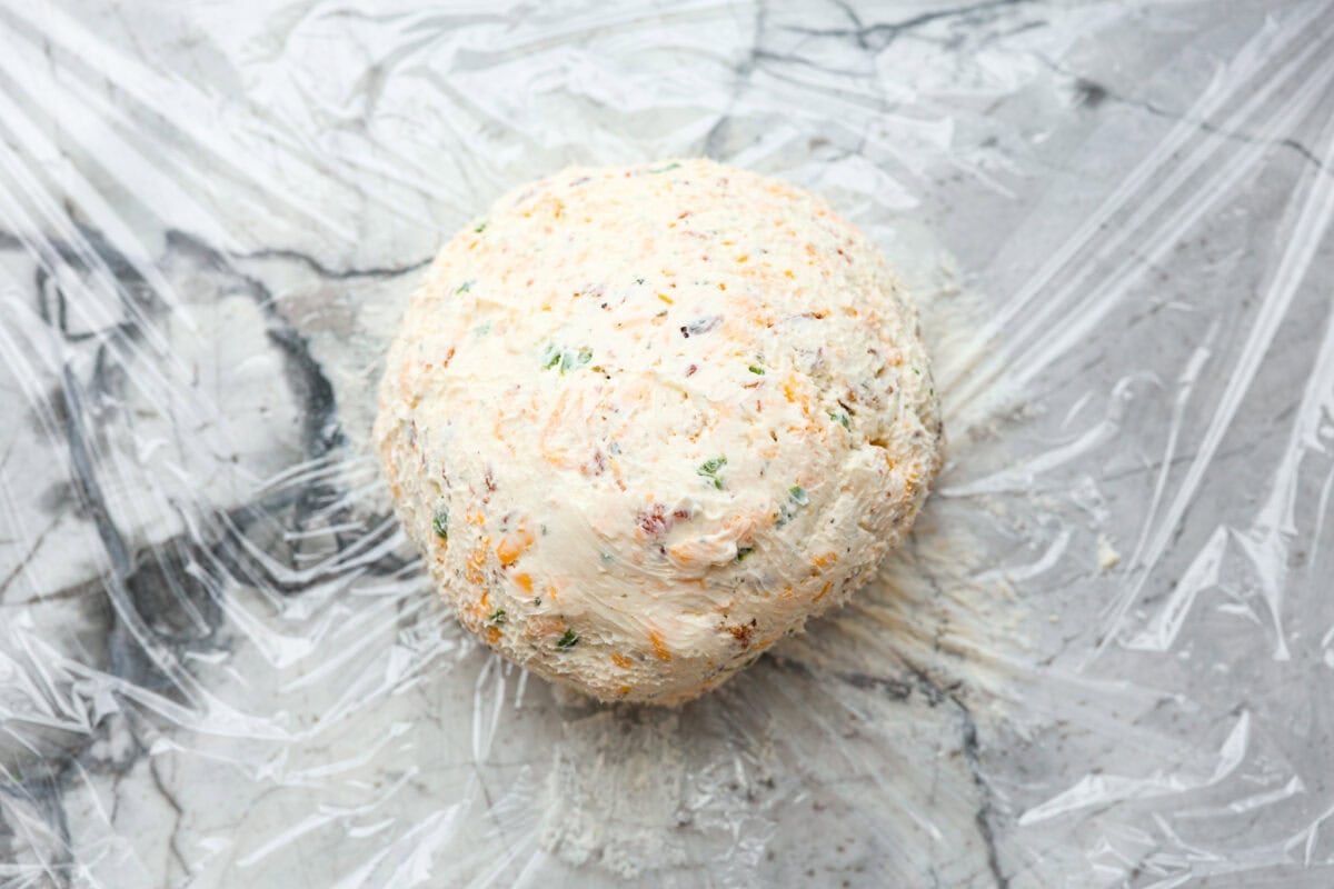 This bacon ranch cheese ball will be your favorite go-to appetizer! The winning combination of bacon, ranch seasoning, and cheddar cheese really stands out in this tasty cheese ball. Serve with crackers and watch everyone devour it! Fourth photo of the cheese ball formed into a ball.