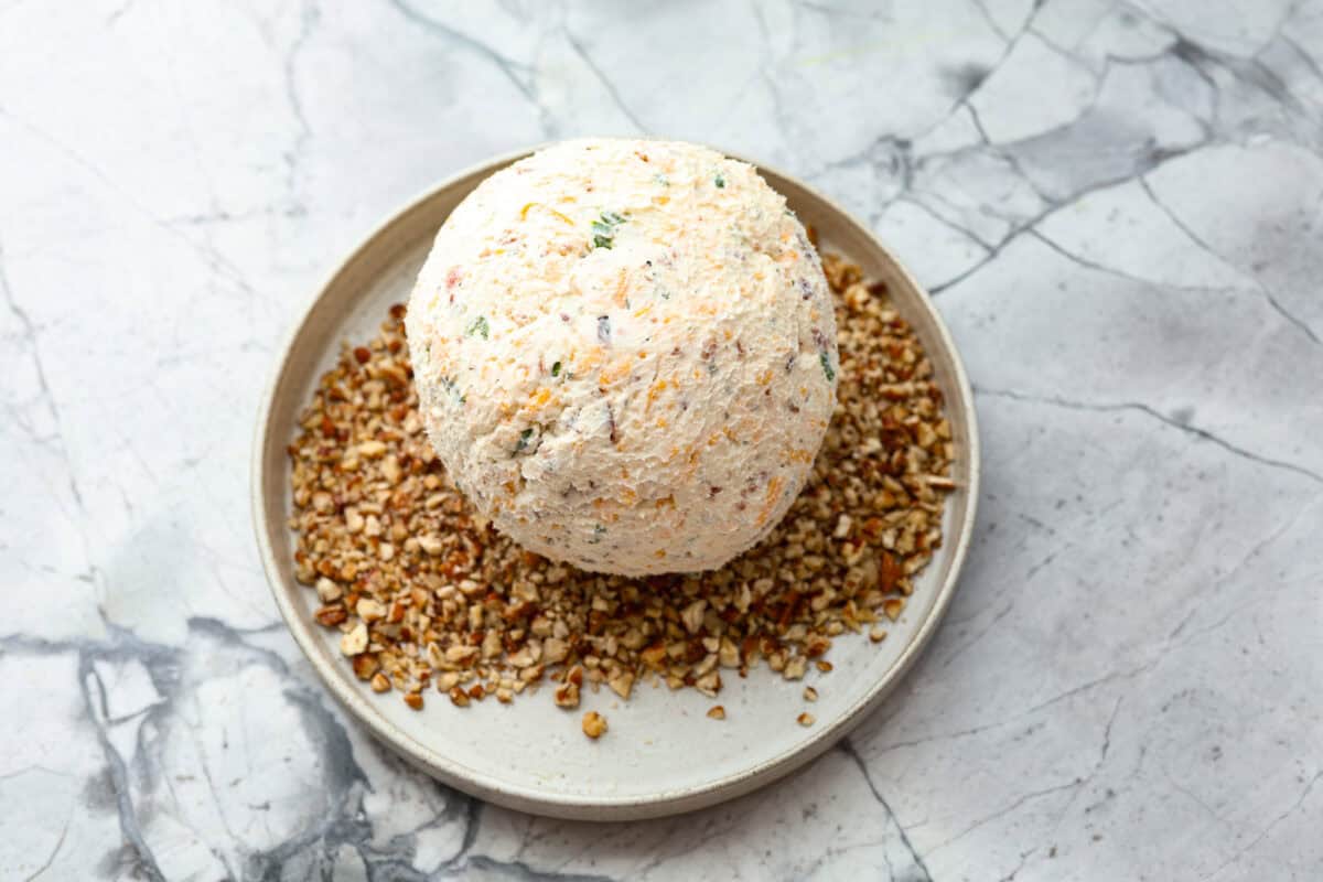This bacon ranch cheese ball will be your favorite go-to appetizer! The winning combination of bacon, ranch seasoning, and cheddar cheese really stands out in this tasty cheese ball. Serve with crackers and watch everyone devour it! Fifth photo of the cheese ball rolling in pecans.