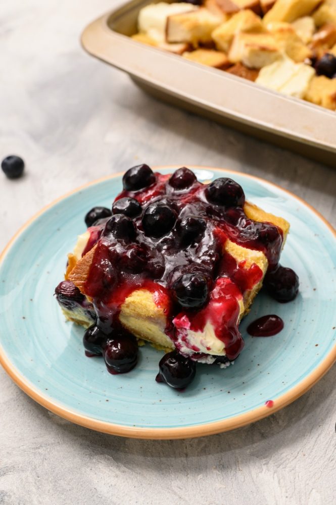 Overnight blueberry French toast on a blue plate topped with blueberries. 