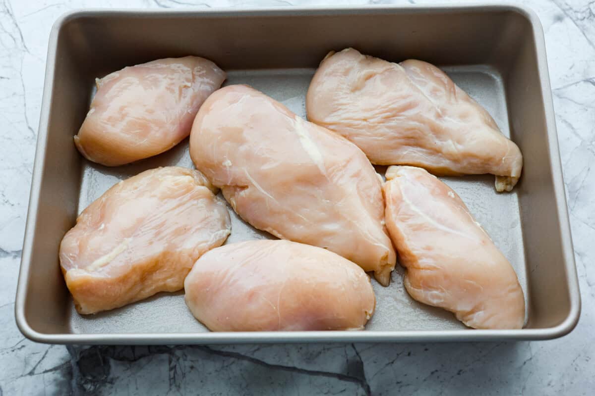 Parmesan baked chicken is so tender and juicy on the inside with a wonderful cheesy exterior. Your family will love the intense flavors, and you will love how quickly and easily this comes together! With only six ingredients and 10 minutes of prep, dinner will be served in no time! Overhead shot of chicken breasts in a 9x13 pan.