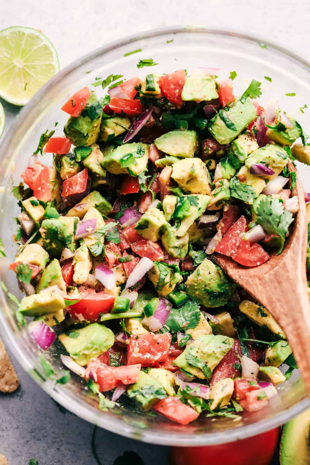 The colors in this dip are so bright and appetizing and the flavors do not disappoint! A close up photo of the california avocado dip with a wooden spoon in the mixture and a lime laying beside the bowl.