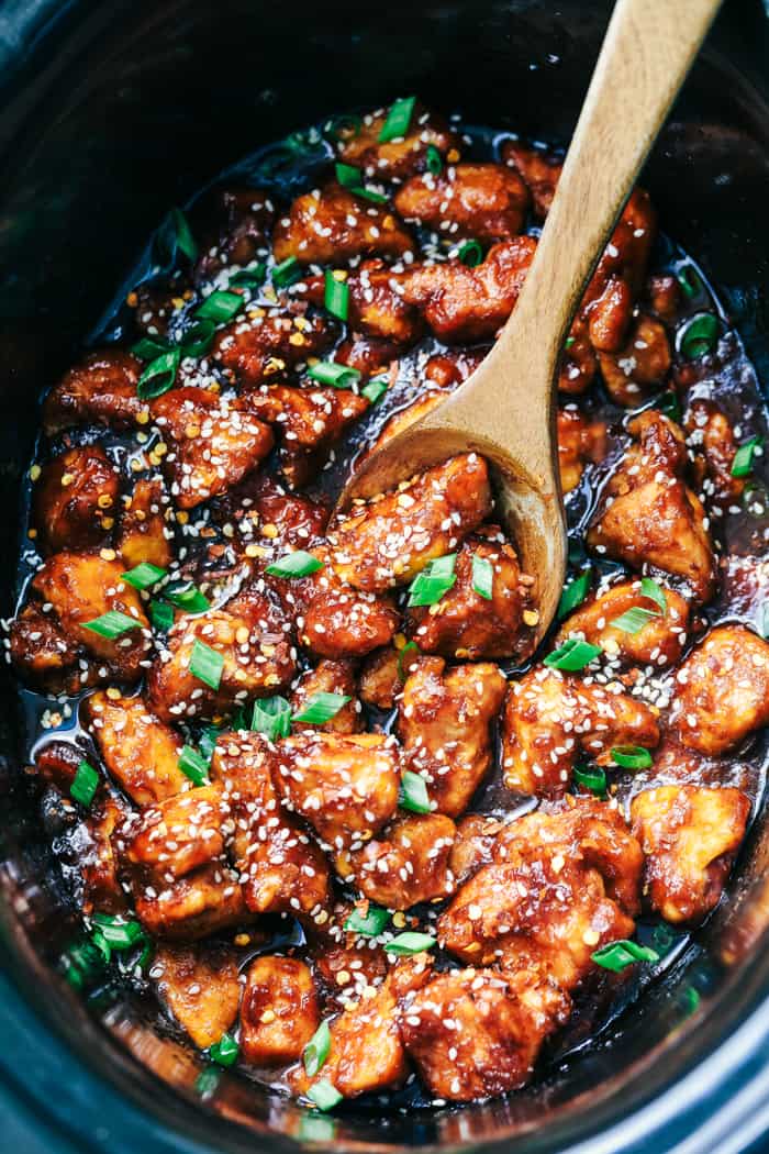 Slow cooker General Tso's chicken is a super easy version of everyone's favorite Chinese entree! Crispy chicken cooked in a sweet and savory sauce with a little added heat. This is way better than takeout! Slow cooker General Tso's chicken in a slow cooker with a wooden spoon.