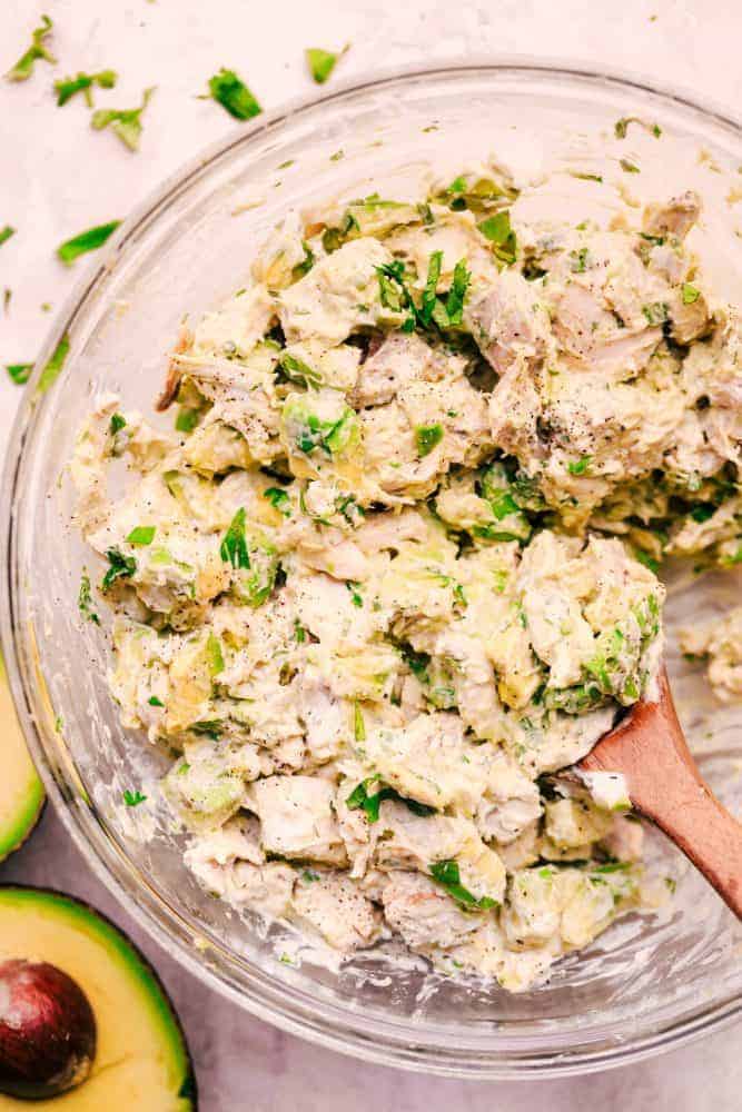 Avocado Chicken Salad is easy to make and you will never want to make your chicken salad without avocado again! Perfect on a sandwich, croissant or served with tortilla chips! Avocado Chicken Salad in a clear bowl with a wooden spoon.
