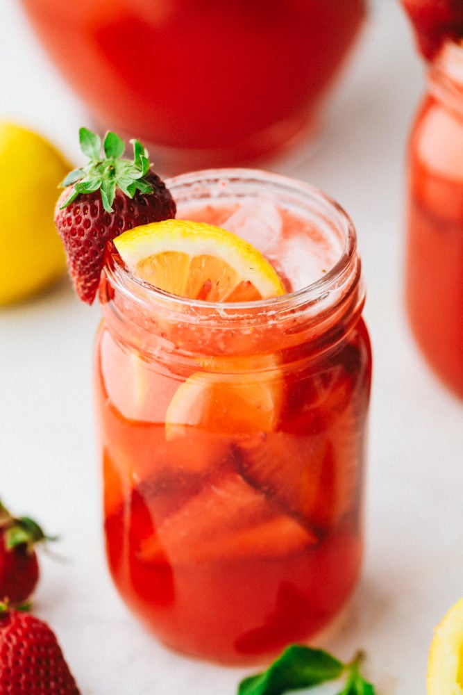 Strawberry lemonade is the perfect summertime drink that is refreshing and delicious! With only a few ingredients, this homemade lemonade will be made quickly and easily! Strawberry lemonade in a mason jar garnished with more fresh strawberries, a lemon slice and a strawberry cut on the side.