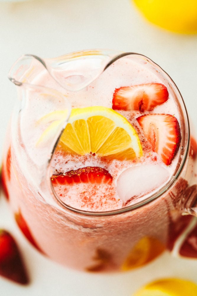 Strawberry lemonade is the perfect summertime drink that is refreshing and delicious! With only a few ingredients, this homemade lemonade will be made quickly and easily! A top photo overview of a pitcher with homemade strawberry lemonade garnished with fresh cut lemons and strawberries.